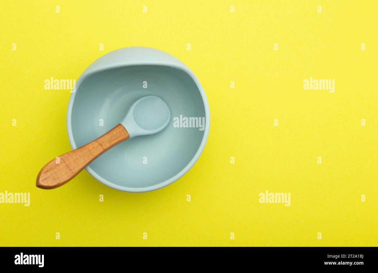 Blauer Kinderteller mit einem Löffel auf gelbem Hintergrund, Nahaufnahme. Babynahrung und Kalorien zum Frühstück, Mittag- und Abendessen. Kopierraum für Text, Comp Stockfoto