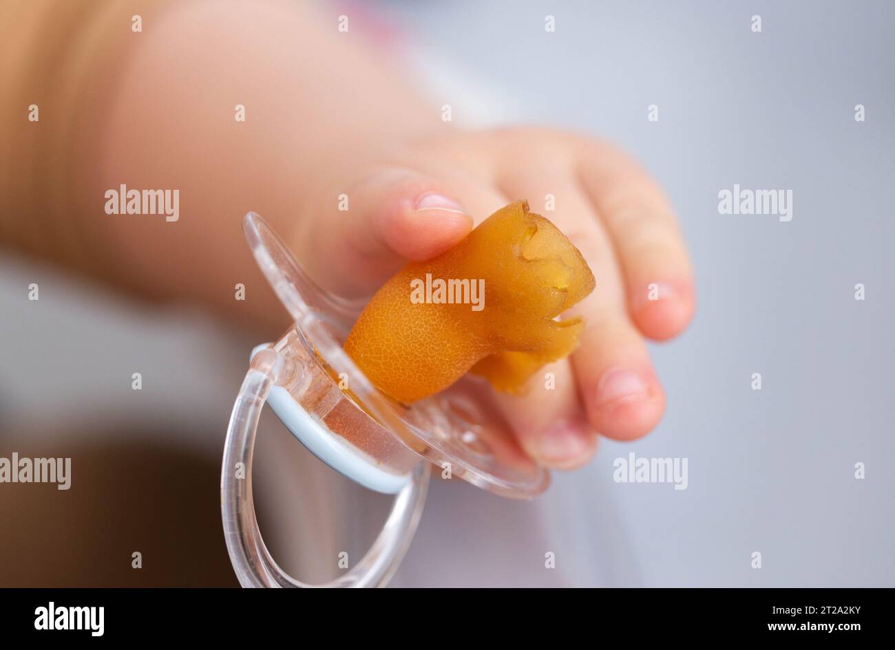 Der Schnuller eines Babys wird gekaut und in der Hand eines Babys zerrissen, Nahaufnahme. Kinderzahnkonzept, Probleme mit Biss. Kopierraum für Text, Silikon Stockfoto