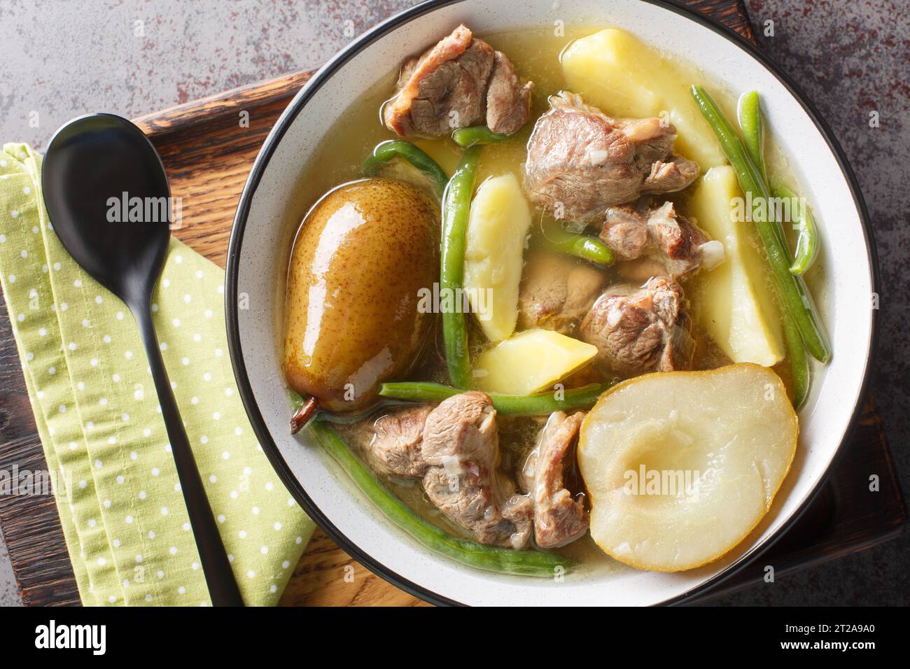 Lammeintopf mit Birnen, Kartoffeln, grünen Bohnen in einer scharfen Soße in einer Schüssel auf einem Holzbrett. Horizontale Draufsicht von oben Stockfoto