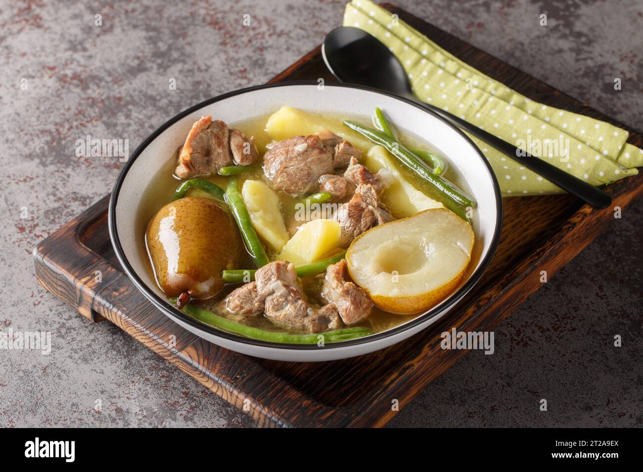 Lammeintopf mit Birnen, Kartoffeln, grünen Bohnen in einer scharfen Soße in einer Schüssel auf einem Holzbrett. Horizontal Stockfoto