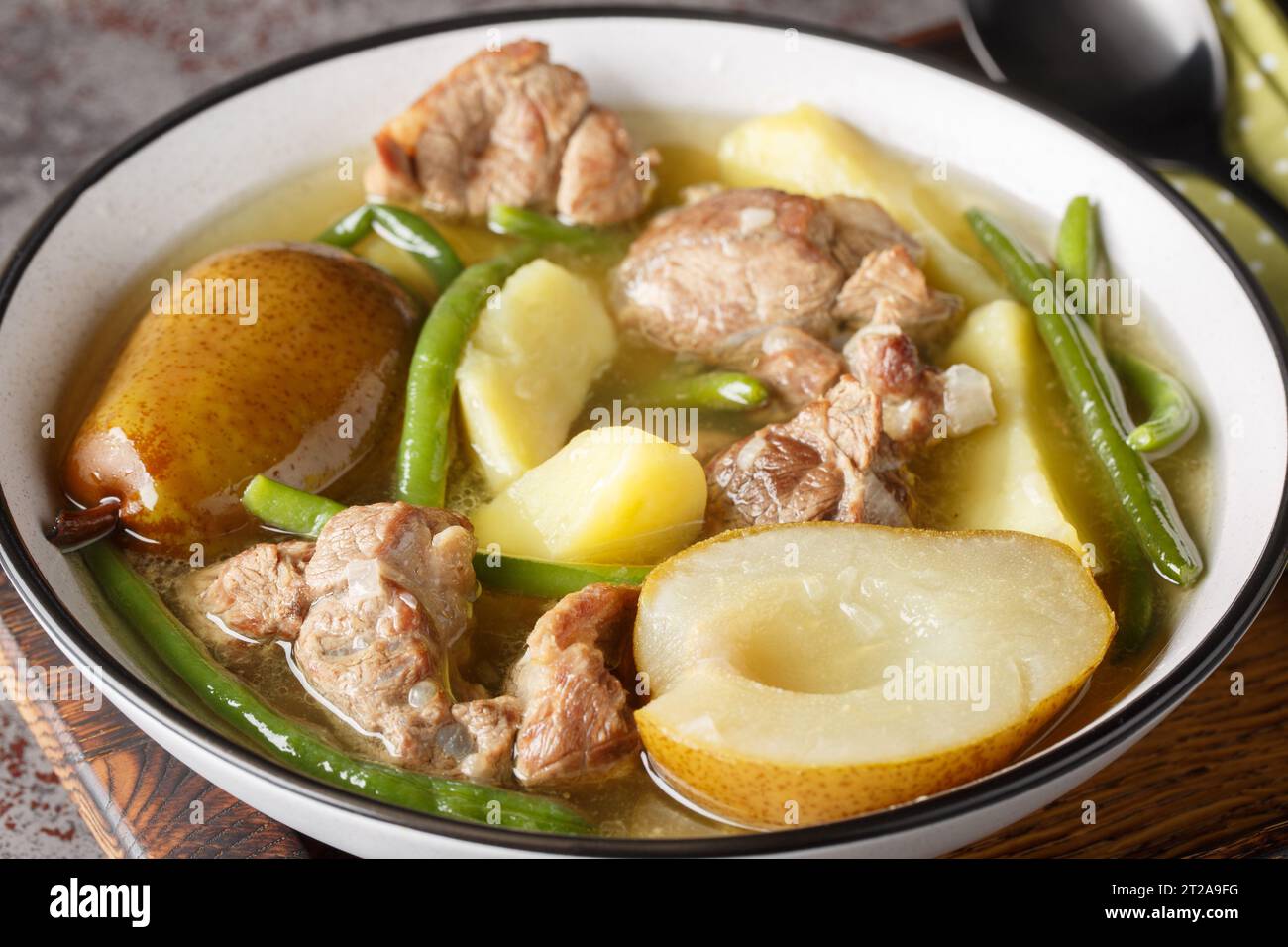 Hammelragout mit Birnen, Kartoffeln, Zwiebeln und grünen Bohnen auf dem Teller auf dem Tisch. Horizontal Stockfoto