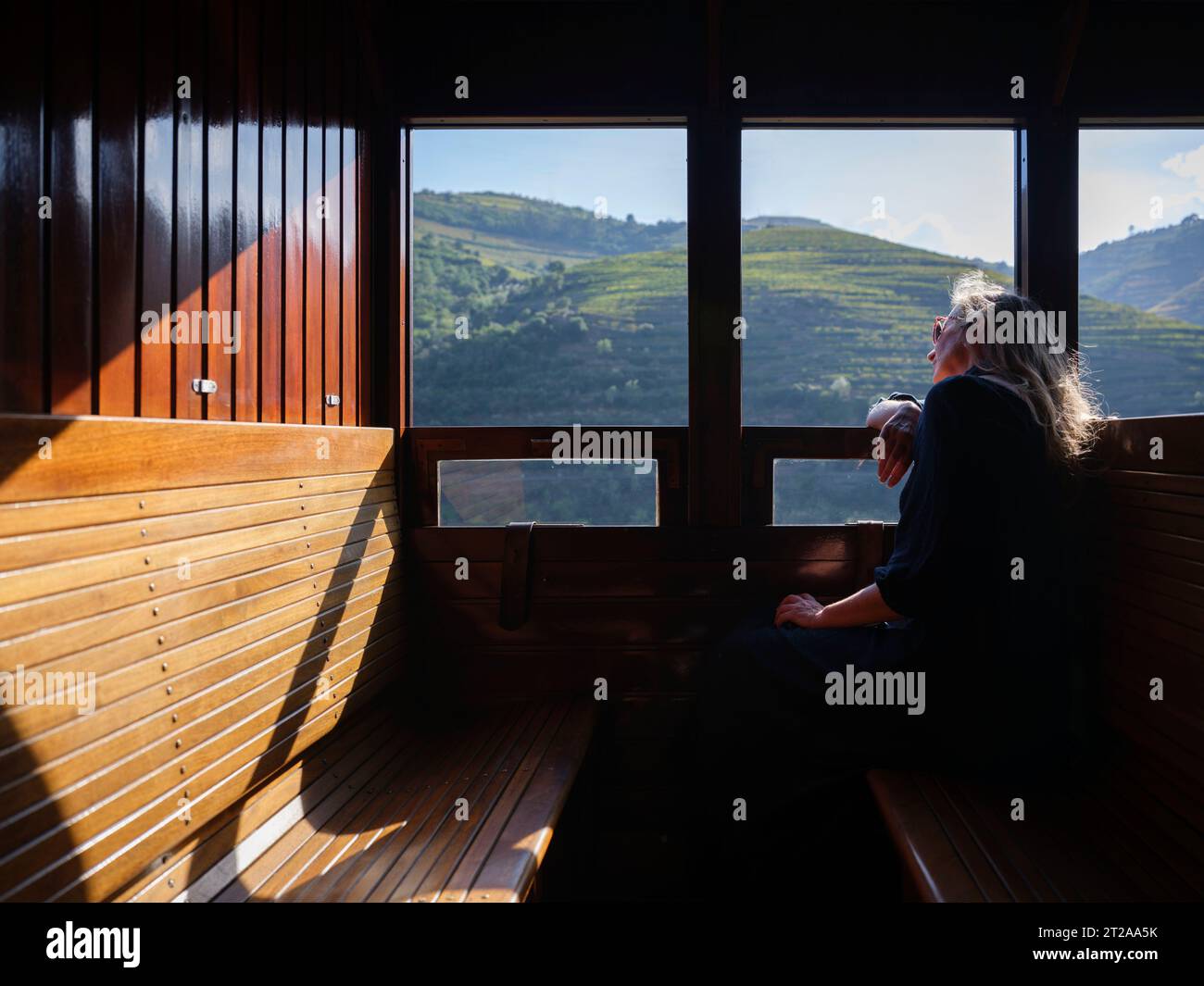 Frau, die allein mit dem historischen Zug von Douro fährt, während sie aus dem Fenster auf die Landschaft entlang des Flusses Douro, Portugal, blickt Stockfoto