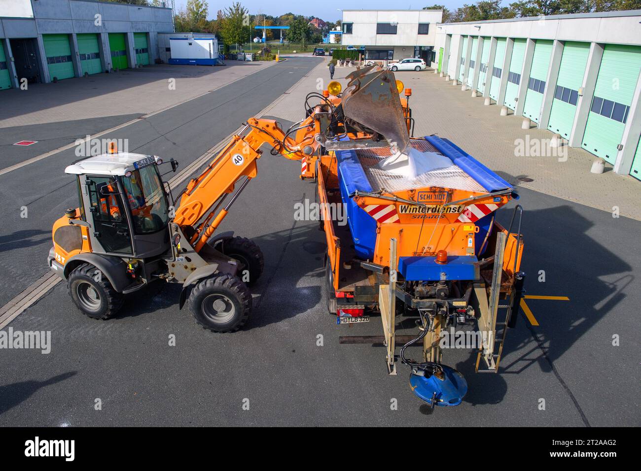 18. Oktober 2023, Sachsen-Anhalt, Staßfurt: Ein Radlader (l) aus dem Bauwerk Atzendorf lädt ein Räumfahrzeug mit Streusalz. Die Straßeninstandhaltungsbehörden in Sachsen-Anhalt haben für den kommenden Winter rund 28.000 Tonnen Salz und 1.800 Tonnen Salzsole gelagert. Im Bundesstaat sind 770 Einsatzkräfte und 289 Räumer- und Streufahrzeuge für den Winterdienst bereit. Das verwendete Streusalz stammt aus Bernburg und kann daher bei Bedarf innerhalb kurzer Zeit geliefert werden. Foto: Klaus-Dietmar Gabbert/dpa Stockfoto