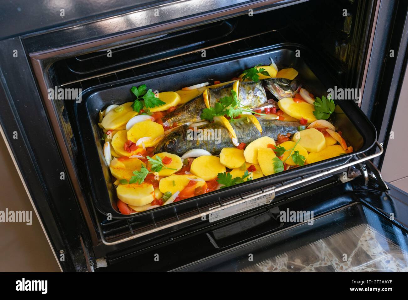 Köstliche rohe Makrele mit Kartoffeln und Tomaten, Zwiebeln, Zitronen und Gewürzen in einem Gericht, das in den Ofen gestellt wird Stockfoto