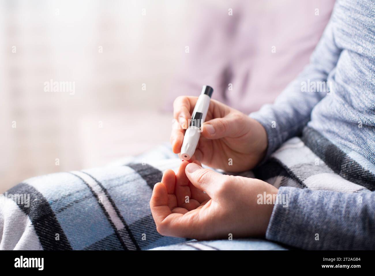 Ein kaukasischer Mann im mittleren Alter sitzt auf dem Sofa und pierct sich seinen Finger mit Lanzette für den Glukosetest Stockfoto