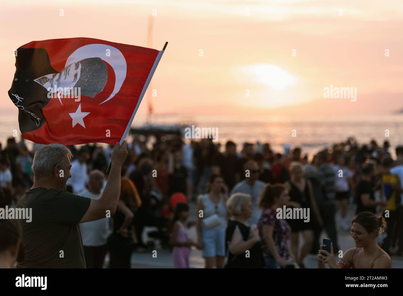 Izmir, Türkei, 9. September 2023, ein Mann mittleren Alters schwingt stolz eine türkische Flagge mit Atatürks Porträt vor einer atemberaubenden Kulisse bei Sonnenuntergang. In t Stockfoto
