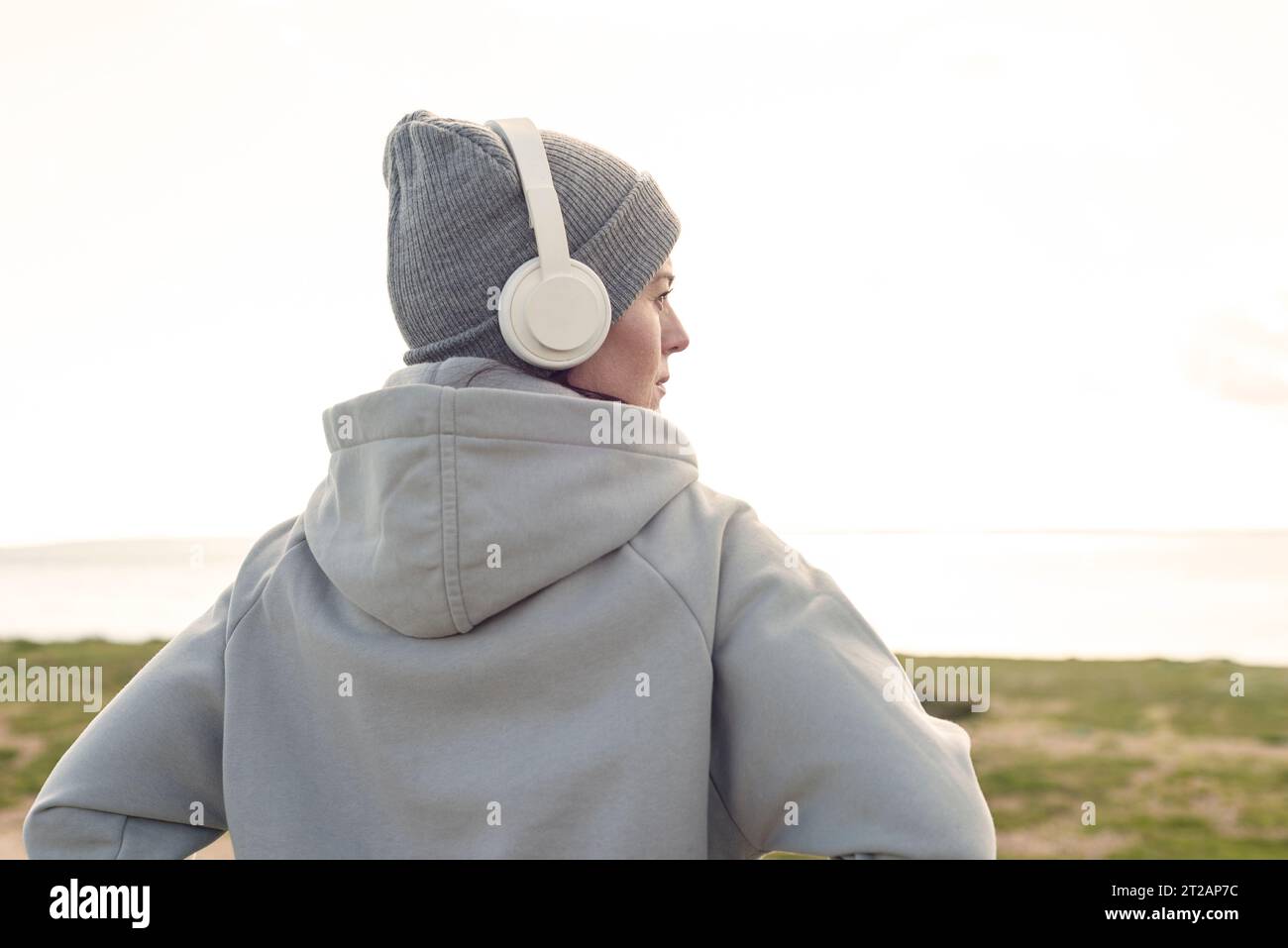 Frau mit Kopfhörern und Wollmütze, die Musik hört und die Aussicht draußen genießt. Lifestyle-Konzept im Winter. Stockfoto