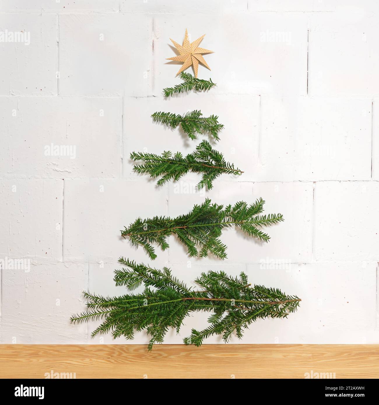 Hausgemachte Weihnachtsdekoration aus natürlichen Zweigen, die horizontal an die Wand genagelt sind, und einem Papierstern als oberes, einfaches und nachhaltiges Tannenalter Stockfoto