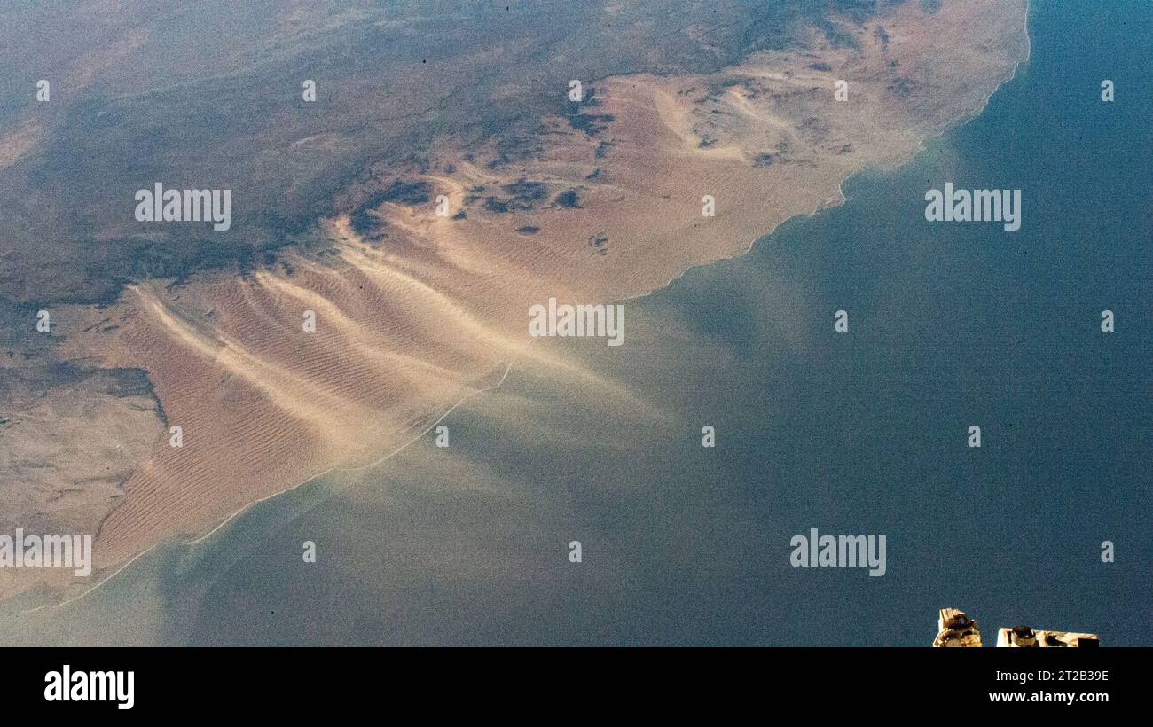 Vom Wind verwehter Sand driftet über die Namib-Wüste an Namibias Atlantikküste in den Ozean, der am 12. September 2023 von der Internationalen Raumstation in 266 Meilen Höhe gefangen wurde. Stockfoto