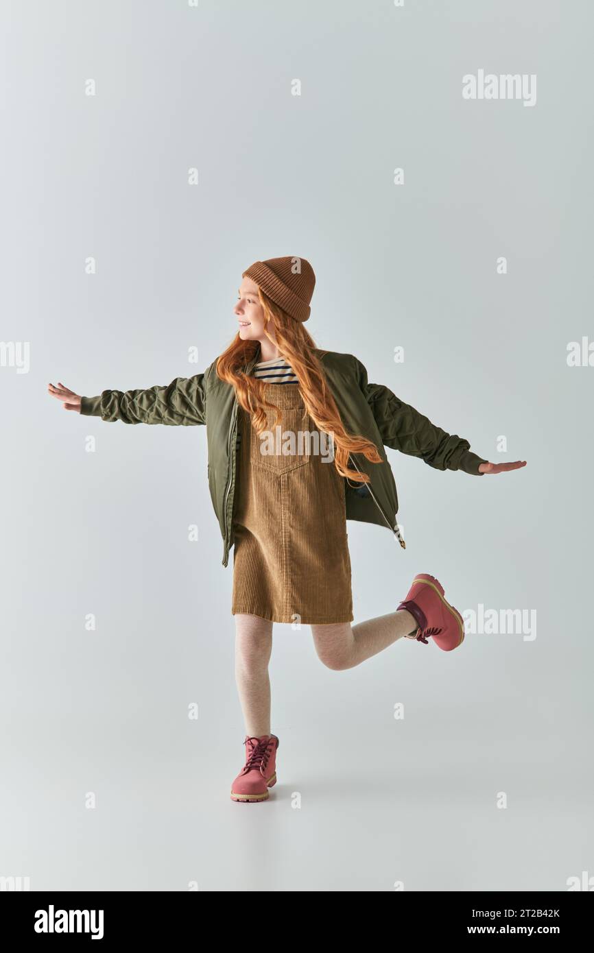 Voller Aufregung im Winter-Outfit und Strickmütze mit ausgestreckten Händen auf Grau Stockfoto