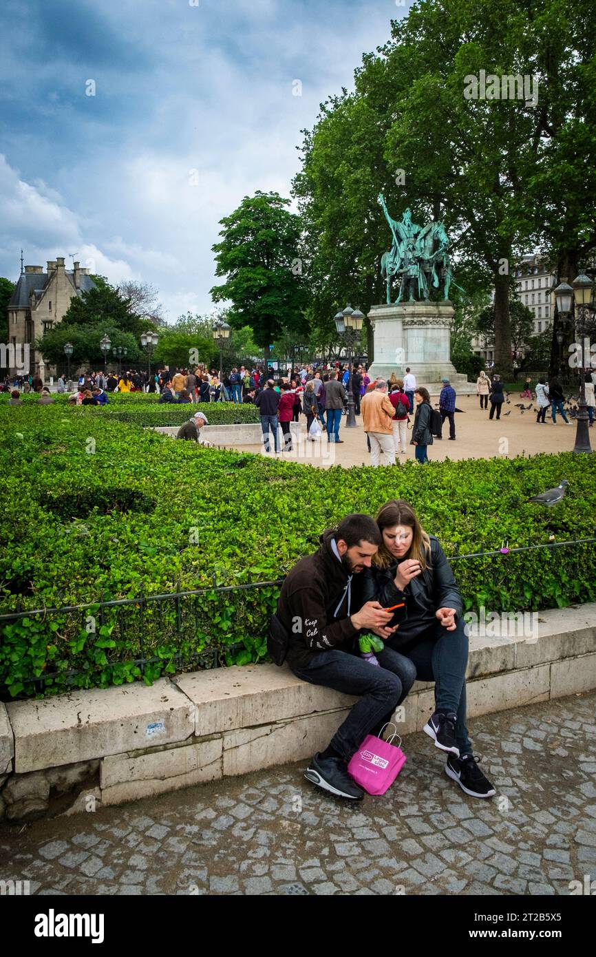 Ein junges Paar schaut sich ein Handy an, während viele Leute über eine Wahrzeichen-Statue in Paris, Frankreich, herumwühlen. Stockfoto