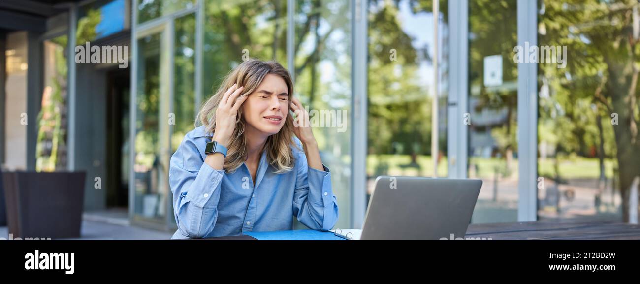 Enttäuschte junge Geschäftsfrau, die sich frustriert fühlte, mit einem Laptop draußen auf der Straße saß, aufschaute und sich beschwerte Stockfoto