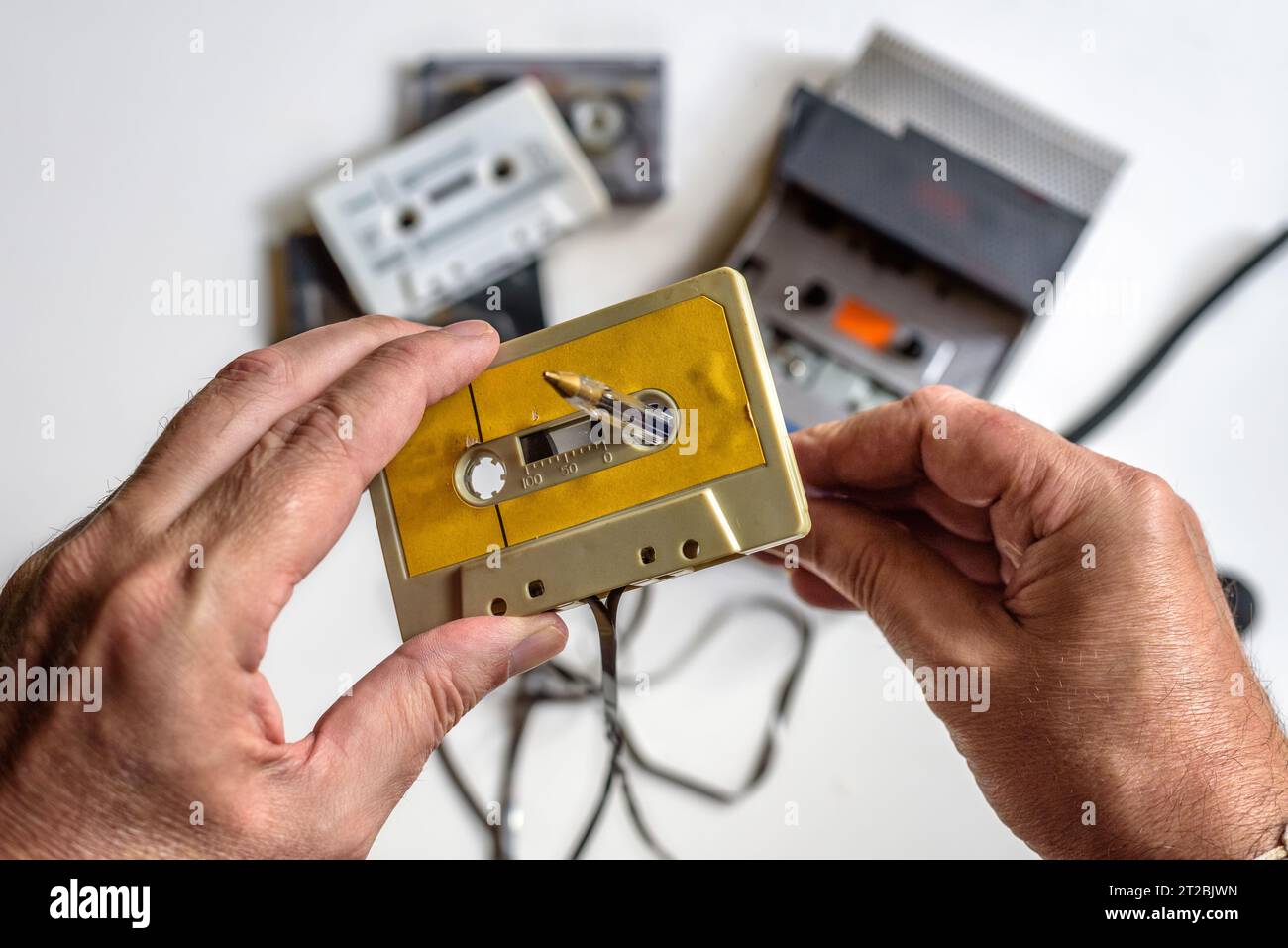 Manuelles Zurückspulen einer Kassette mit Hilfe eines Stifts, eines Kassettenspielers und mehrerer Bänder auf weißem Hintergrund. Stockfoto