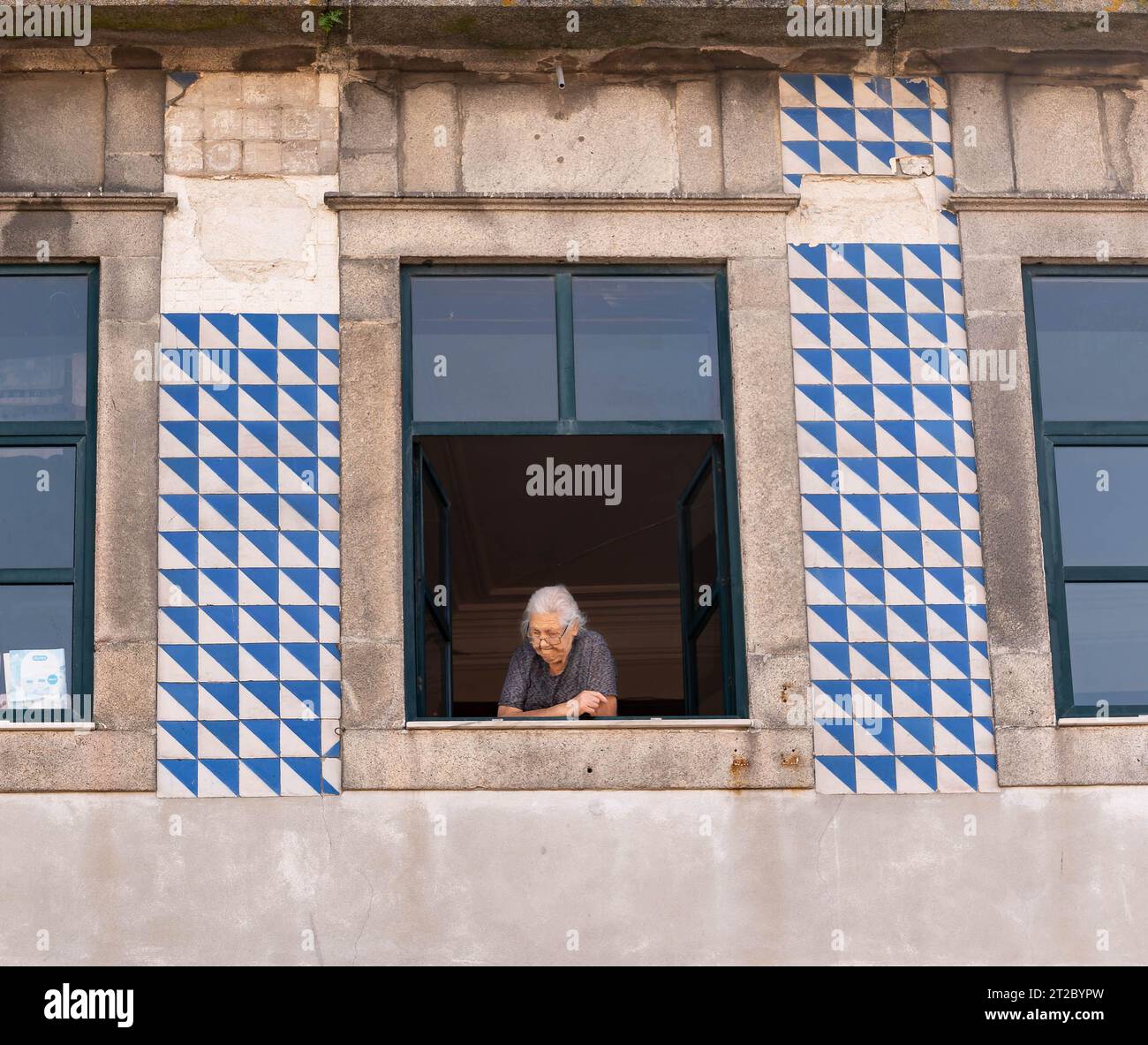 Ältere portugiesische Frau am Fenster mit traditionellen blauen und weißen Azulejo-Fliesen in Porto Stockfoto