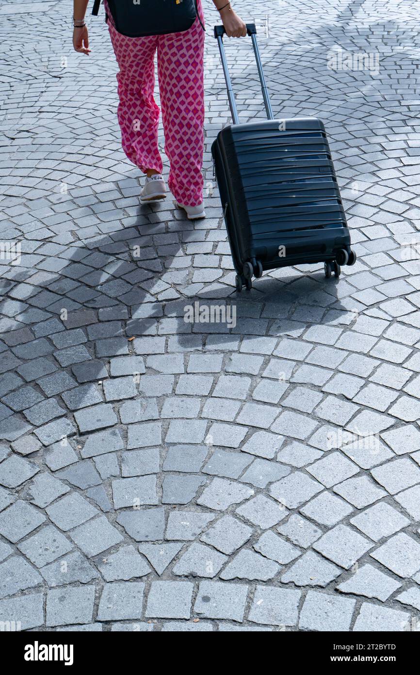 Frau mit rosa gemusterter Hose, die schwarzen Koffer auf der Kopfsteinpflasterstraße in Porto zieht Stockfoto