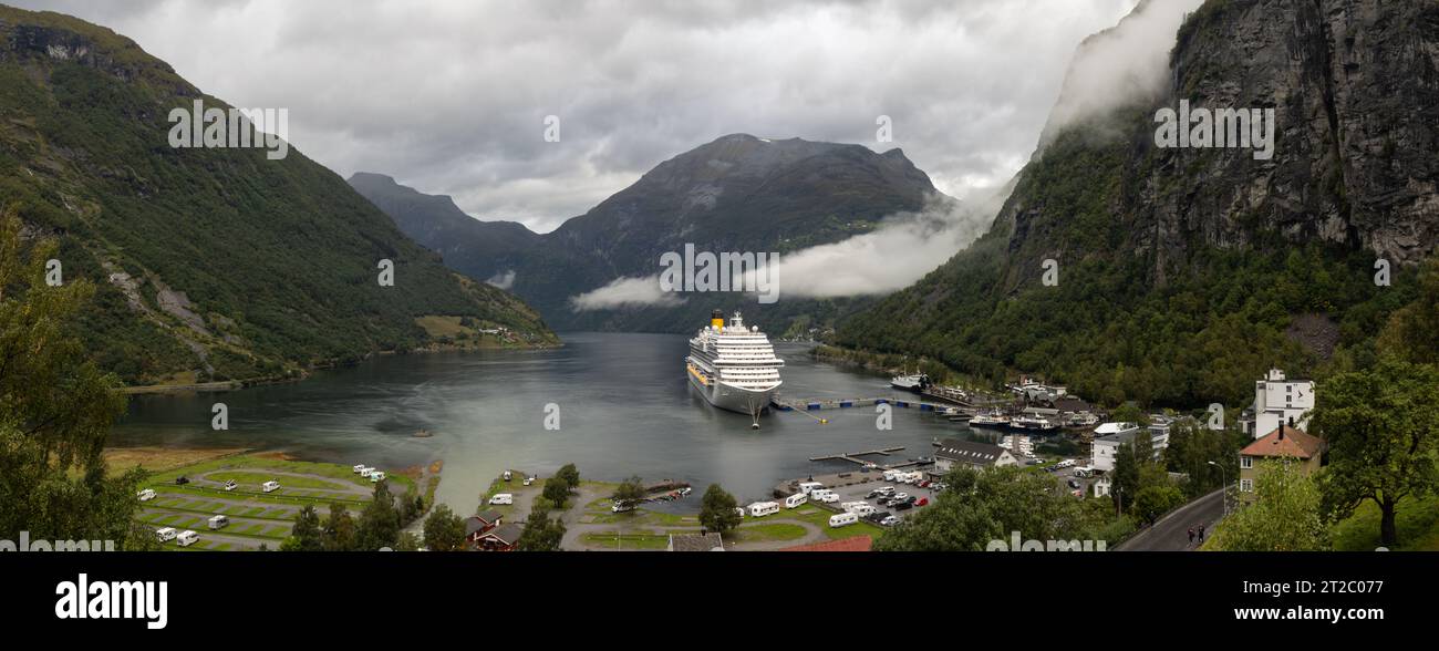 Besondere aussicht panorámica desde la iglesia Octogonal de Geiranger del final del fiordo rodeada de Montañas con nubes bajas, el pueblo y un crucero Stockfoto