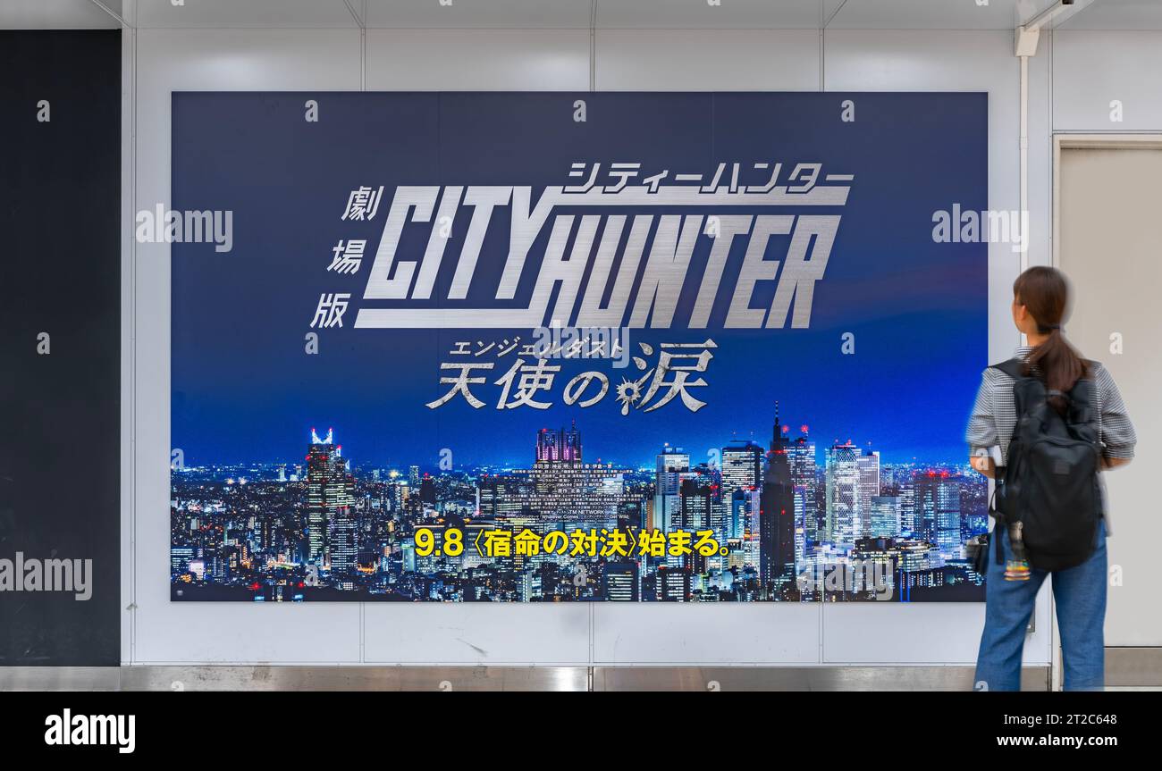 tokio, japan - 08. september 2023: Ein Fußgänger, der ein großes Poster im Bahnhof Shinjuku ansieht, das eine nächtliche Stadtlandschaft von Shinjuku vom Anime City Hunter darstellt Stockfoto