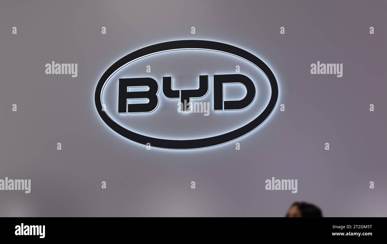 Das Logo von BYD an der Wand des Innengeschäfts. Die Marke BYD Company in einem elektronischen Ausstellungsraum. Ein Teil eines unscharfen Passanten im Vordergrund. Stockfoto