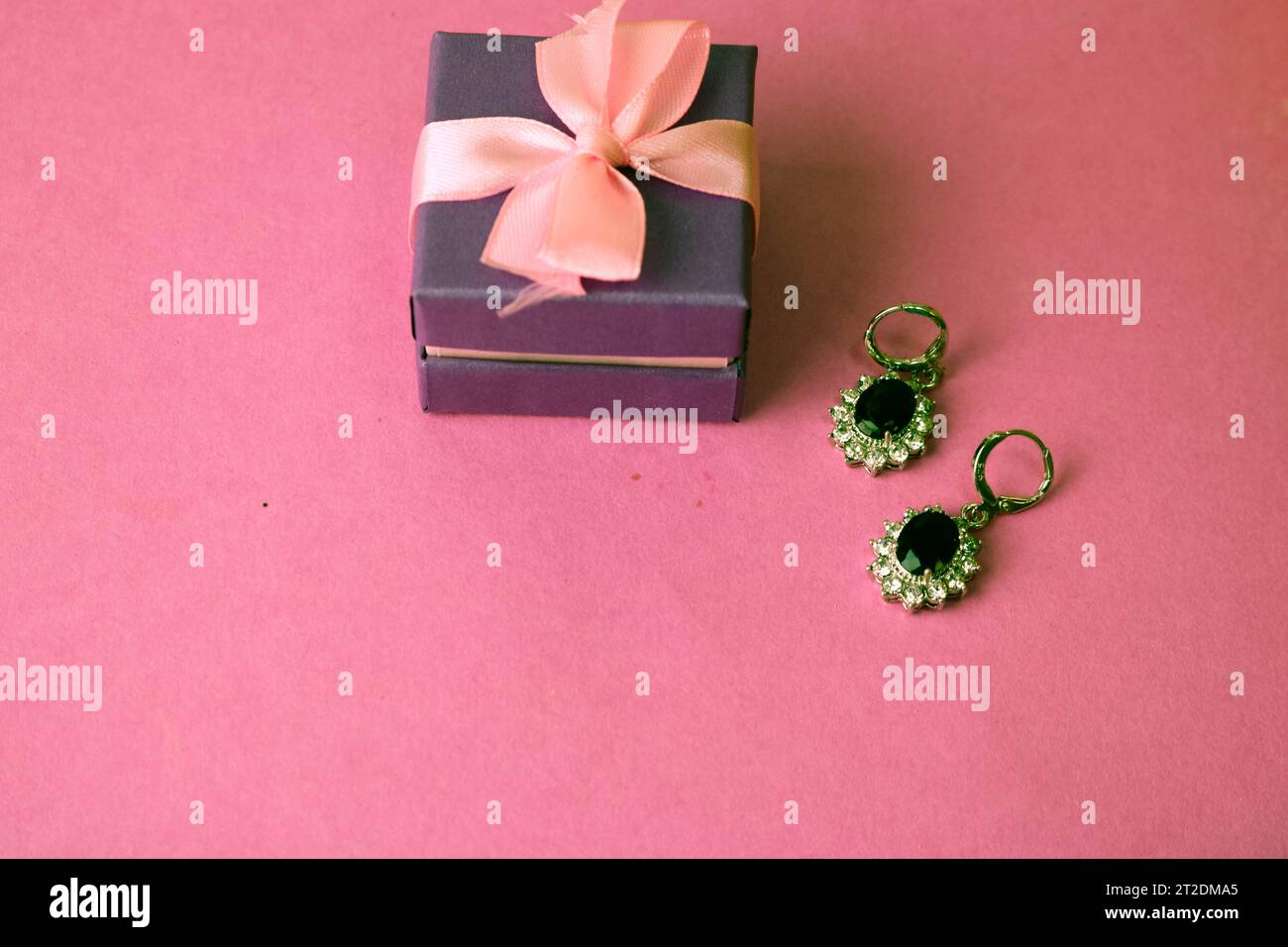 Beauty Box, festliche schöne Geschenkbox mit einer Schleife mit silbernen Ohrringen mit Edelsteinen auf pinkfarbenem lila Hintergrund. Flach verlegt. Draufsicht. Stockfoto