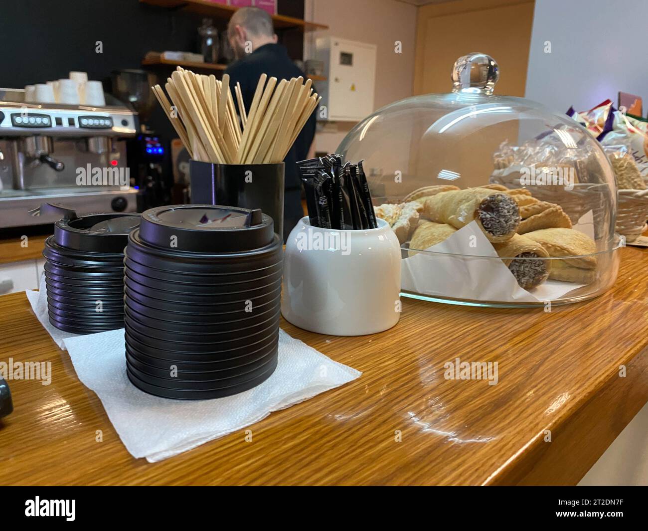 Einweg-Sticks aus Naturholz zum Mischen von Zucker in Tee oder Kaffee, Zuckerschale, Thermodeckel aus Kunststoff für Tassen und Kuchen an der Bar in einem kleinen Café. Stockfoto