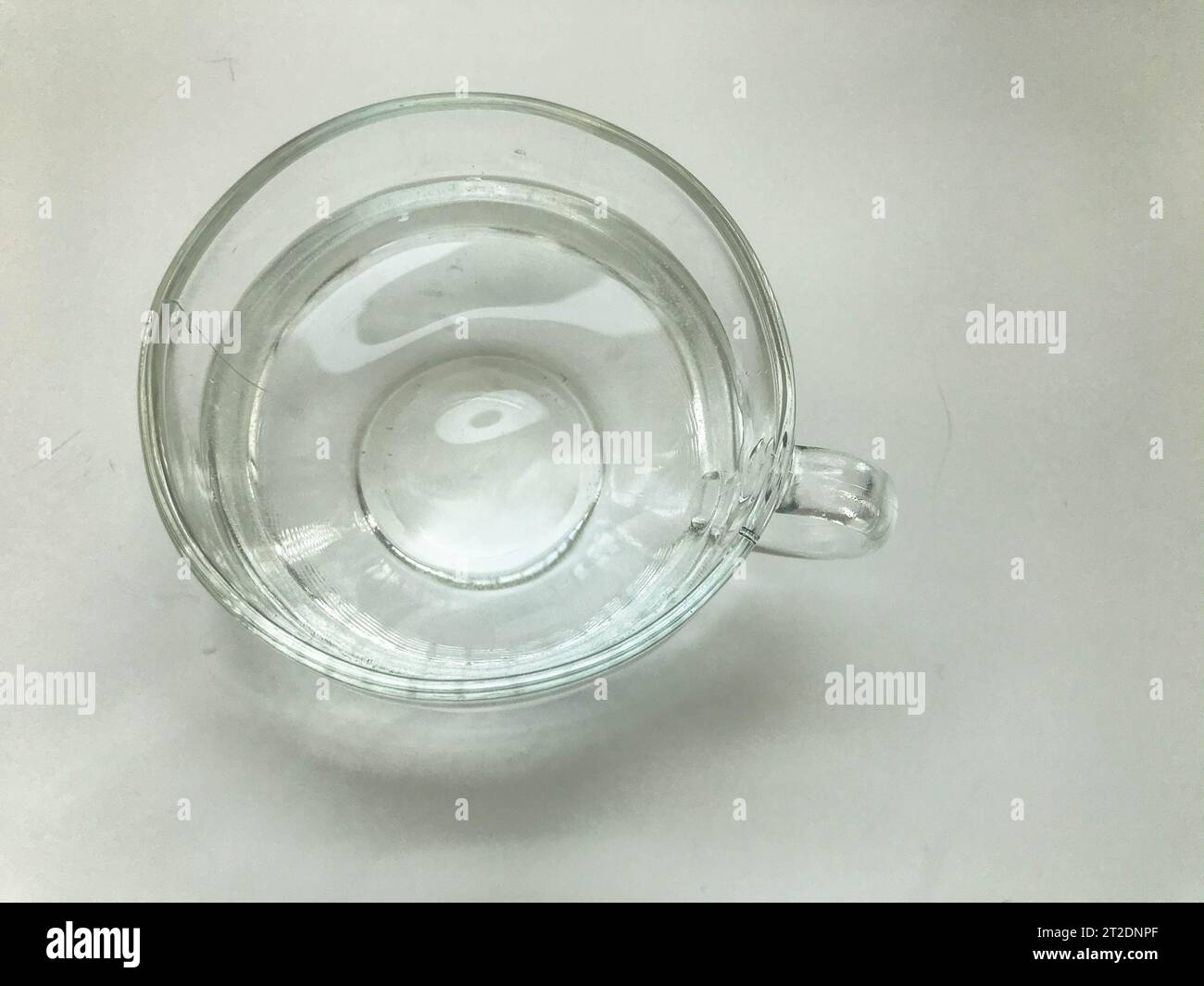 Leerer transparenter Becher, rund und groß, gefüllt mit Wasser. Glasbecher mit rundem Griff. Tee trinken, Kaffee trinken. Becher auf einem weißen, matten Hintergrund Stockfoto