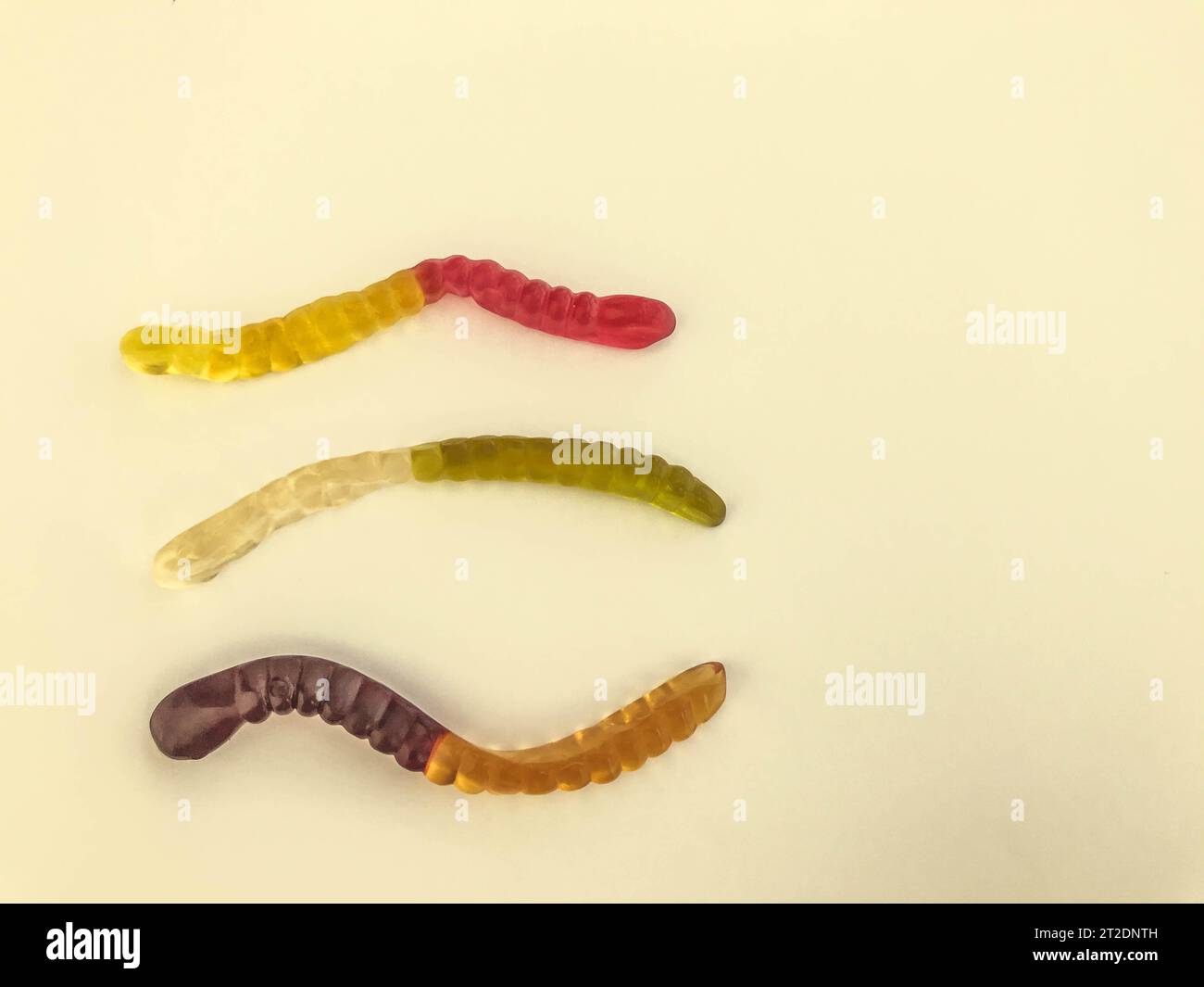Gelatinöse Würmer unterschiedlicher Farben liegen auf einem gelb-matten Hintergrund. Gummibonbons in Form von langen Würmern von heller Farbe. Lecker und appetitlich Stockfoto