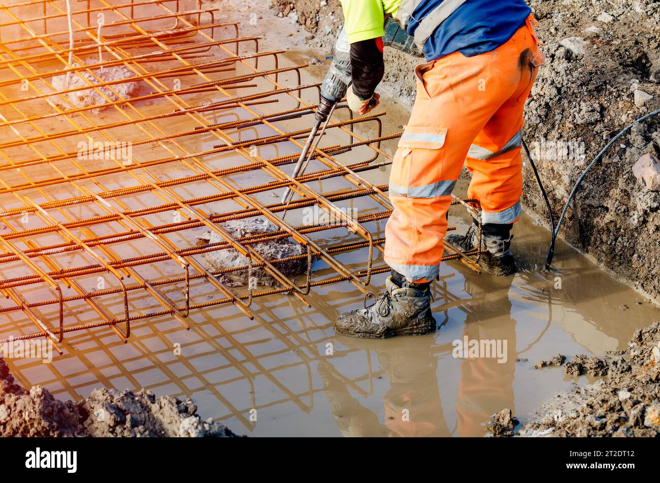Der Baumeister verwendet einen elektrischen Bremser, um Beton von der Oberseite des Stapels zu brechen, um den Bewehrungskäfig darauf zu montieren Stockfoto