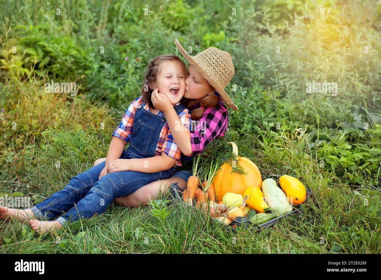 Glückliche Bauernkinder, die in der Nähe der Box sitzen, mit Ernte aus dem eigenen Garten. Saisonale Herbst- und Sommerarbeiten. Bio-Lebensmittel. Gartenprodukte und geerntetes Gemüse Stockfoto