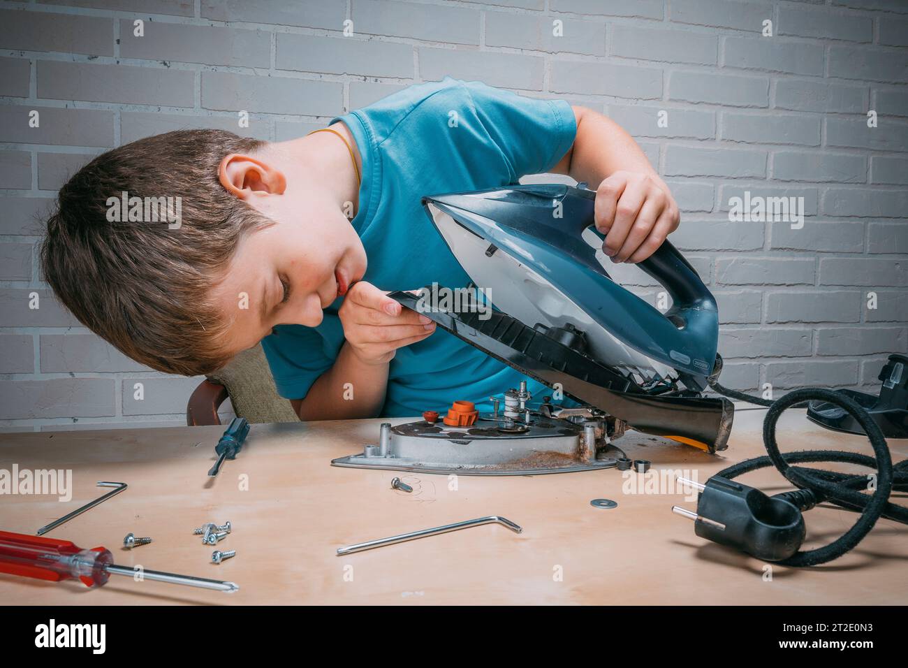 Junge hilft seiner Mutter. Ein lustiger Meister repariert ein Elektroeisen auf dem Tisch mit Werkzeugen. Zerlegtes Elektroeisen. Stockfoto