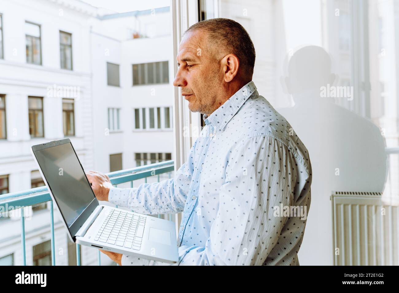 Attraktiver Mann im Hemd steht neben dem Fenster mit Laptop Stockfoto