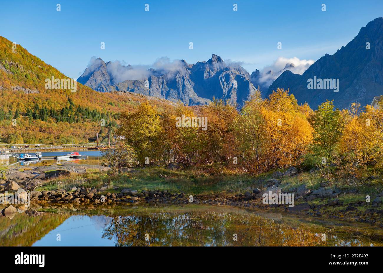 Wunderschöne Landschaft Norwegens mit Bäumen mit gelben Blättern, die sich im Wasser eines Sees spiegeln, und Berggipfeln im Hintergrund Stockfoto