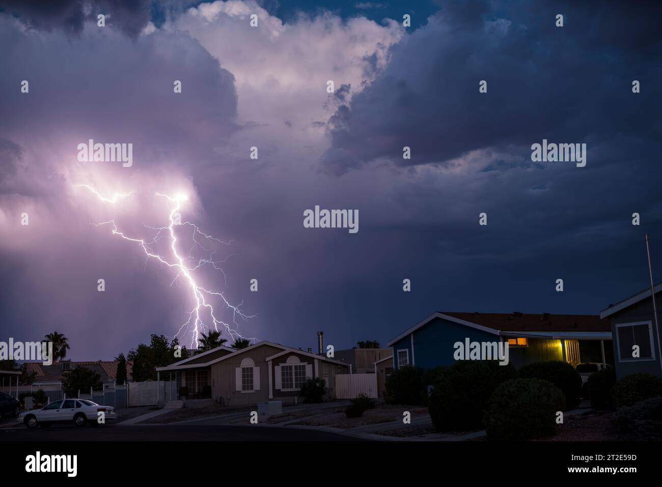 Traumhafte Vision eines Blitzeinschlags direkt hinter einer Nachbarschaft aus unscheinbaren modularen Häusern in der blauen Stunde der Dämmerung. Stockfoto