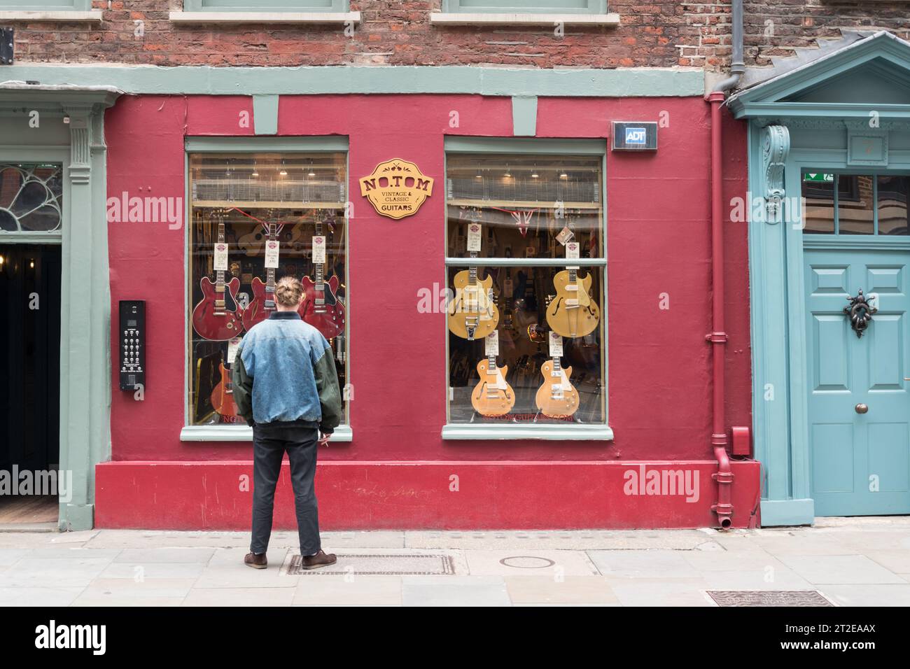 Ein junger Mann in einer Jeansjacke, der bei No. Shoppt Tom Guitars, Denmark Street, London, WC2, England, GROSSBRITANNIEN Stockfoto