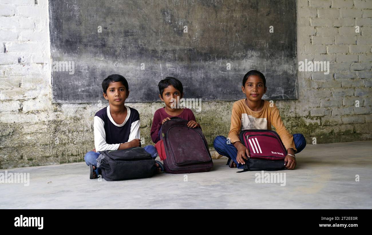 Glückliche indische Grundschüler, die am Schreibtisch im Klassenzimmer sitzen und in Notizbuch mit Bleistift schreiben, Prüfung und Test, weibliche Lehrerin Stockfoto