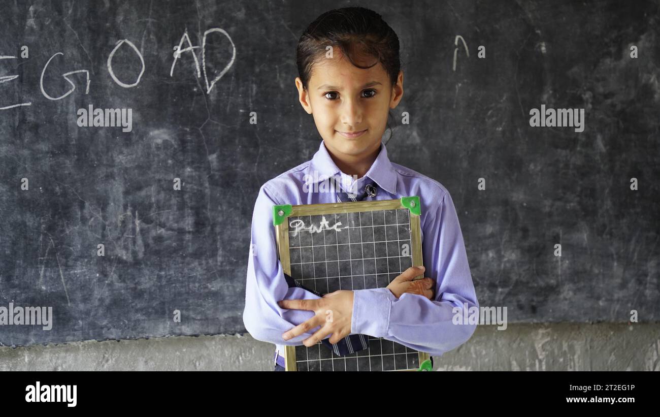 Glückliche indische Grundschüler, die am Schreibtisch im Klassenzimmer sitzen und in Notizbuch mit Bleistift schreiben, Prüfung und Test, weibliche Lehrerin Stockfoto