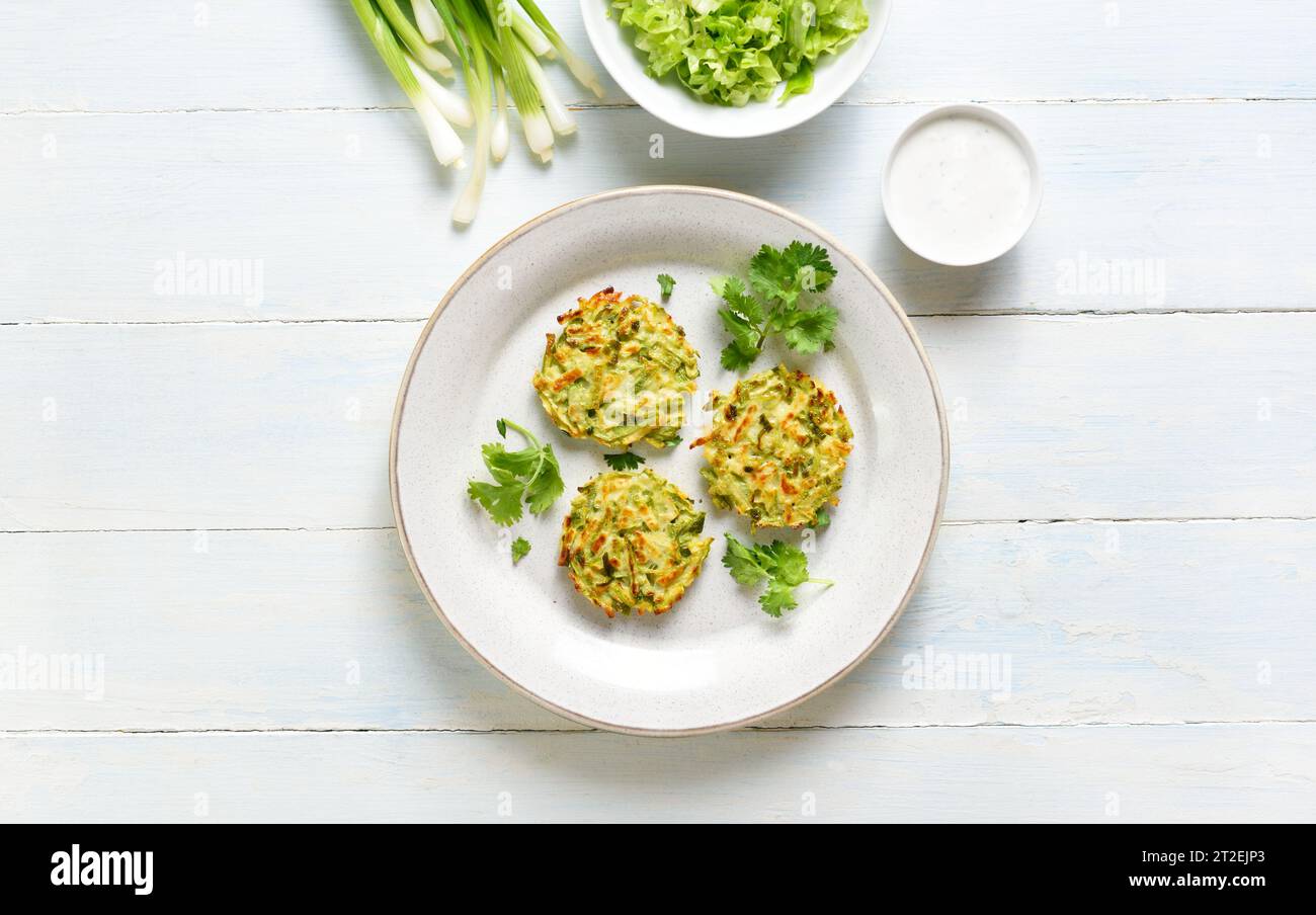 Vegetarische Gemüsezucchini-Pfannkuchen mit grüner Zwiebel auf Teller mit Soße über hellem Holzhintergrund. Draufsicht, flach Stockfoto