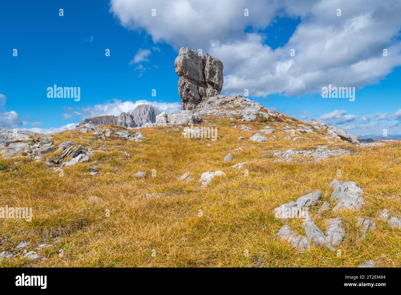 Großer freistehender Kalkstein auf einem kleinen Hügel, der von braunem Gras bedeckt ist, vor blauem Himmel mit Wolken Stockfoto