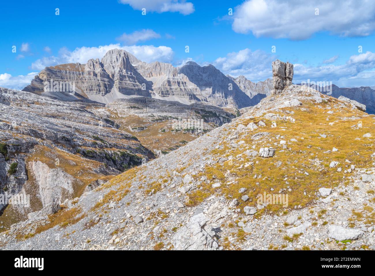 Großer freistehender Kalkstein gegen geschichtete Gebirgszüge in den Brenta-Dolomiten in Italien, Herbstsaison Stockfoto