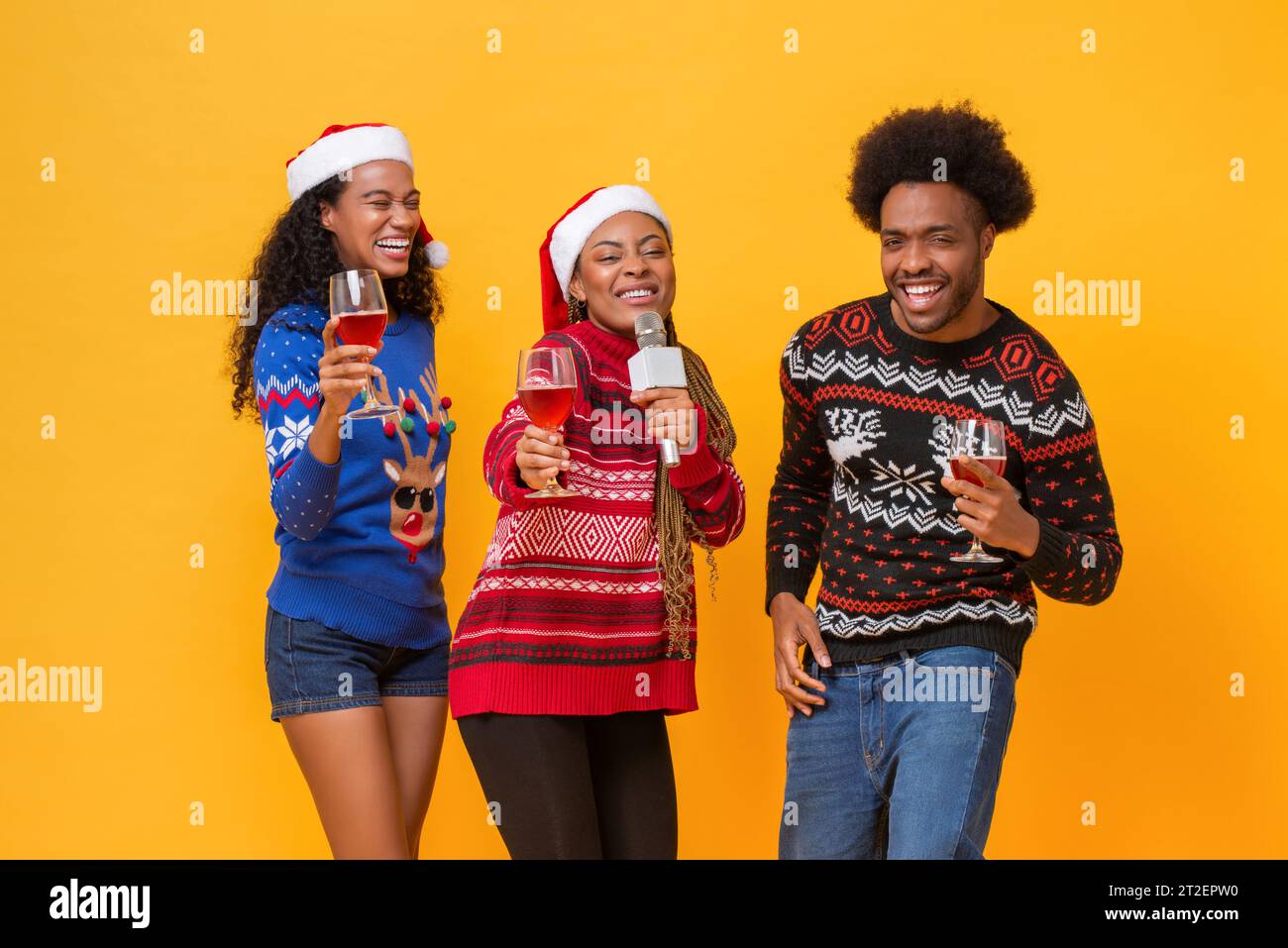 Glückliche, vielfältige Freunde in Weihnachtspullover trinken, singen, feiern und gemeinsam Spaß haben in gelbem isoliertem Hintergrundstudio Stockfoto