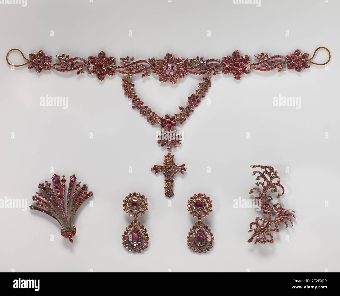 Fünfteilige Parure im Originaletui möglicherweise französisches drittes Viertel 18. Jahrhundert dieses passende Schmuckset, oder Parure, besteht aus verschiedenen Elementen und enthält eine Halskette, ein Paar Ohrringe und zwei Haarschmuck, die im Originaletui aufbewahrt werden. Die in Gold gehaltenen Stücke sind mit facettierten Granaten montiert, die mit rosafarbener Metallfolie unterlegt sind, um ihre Farbe zu verstärken. Granate waren im 18. Jahrhundert sehr modisch und wurden verwendet, um attraktiven und erschwinglichen Schmuck speziell für junge Frauen zu schaffen. Die verschiedenen abnehmbaren Teile, wie der Festoon und der kreuzförmige Anhänger des Nekklac Stockfoto