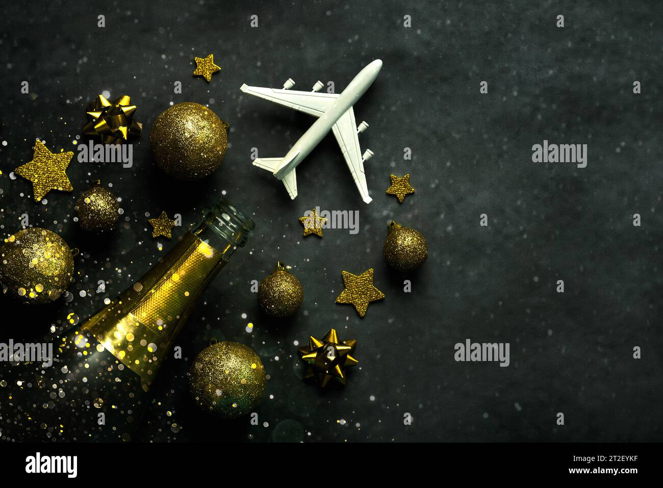 Hintergrund des Weihnachtskonzepts. Sektflasche, weihnachtskugeln, glitzernder Glitzer und Flugzeug mit Platz für Text auf grauem Hintergrund. Weihnachtsreise Co Stockfoto