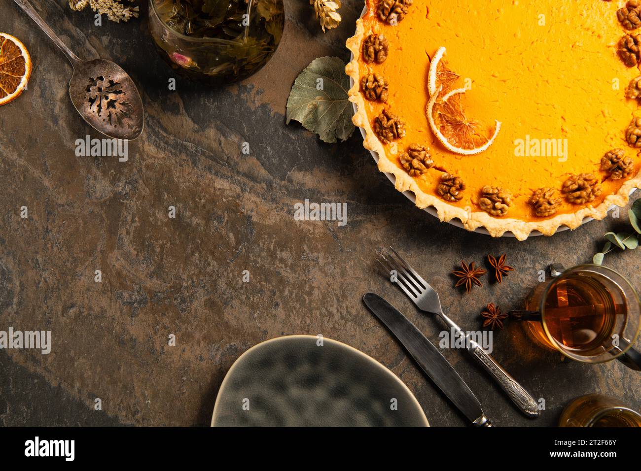 thanksgiving-Komposition, garnierter Kürbiskuchen in der Nähe von Vintage-Besteck, Gewürze und Tee auf Steintisch Stockfoto