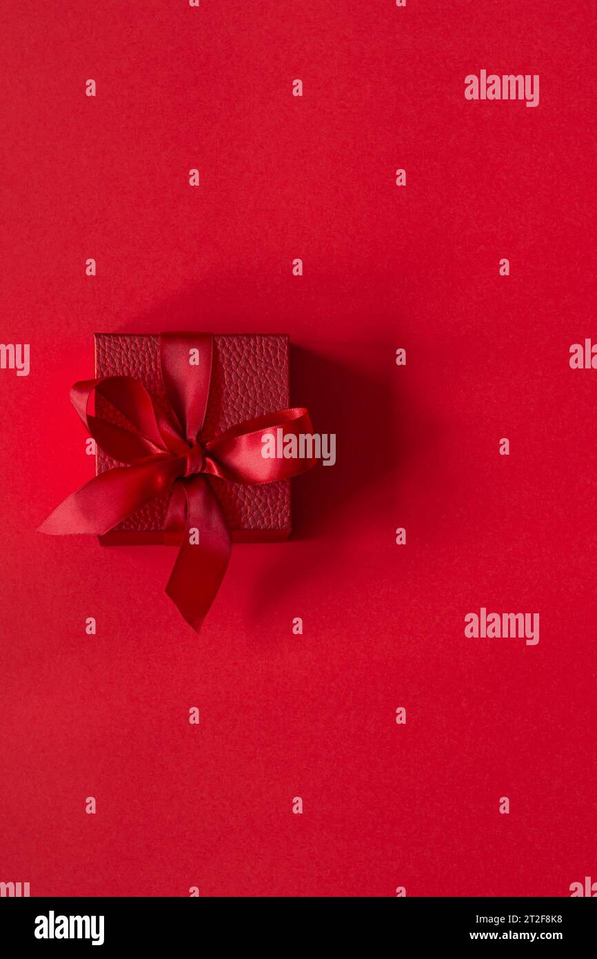 Rote (scharlachrote) Geschenkbox mit Satinband auf rotem Hintergrund. Begrüßungskonzept für Geburtstag, Weihnachten, Valentinstag, Muttertag. Stockfoto