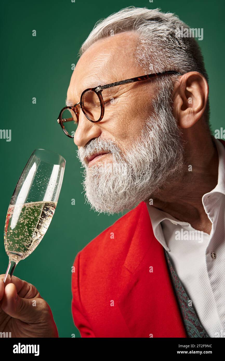Porträt des Weihnachtsmanns mit weißem Bart und Gläsern, die Champagner vor grünem Hintergrund genießen, Winterkonzept Stockfoto