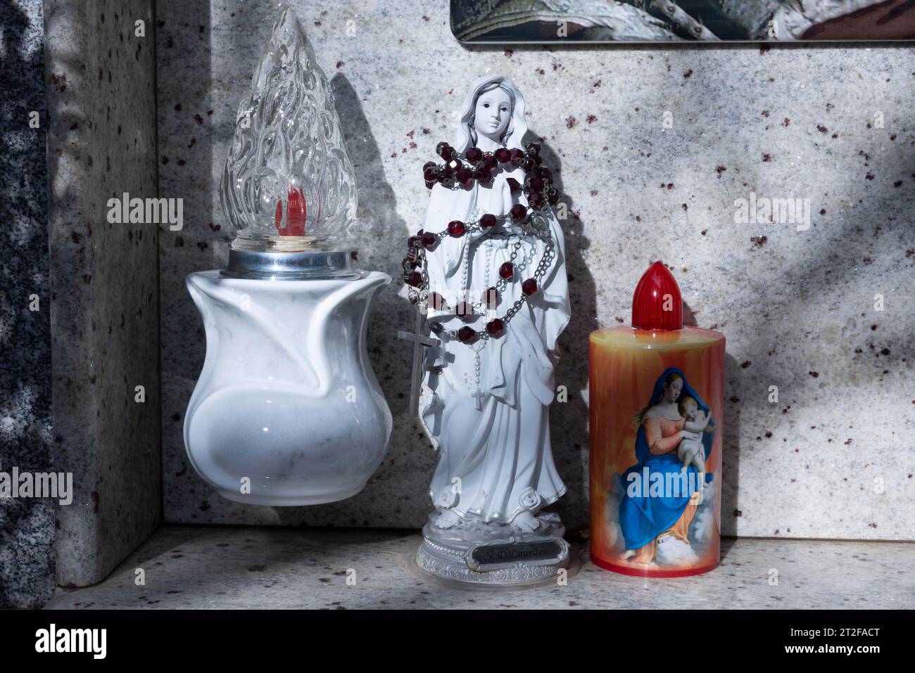 Kitschige elektrische batteriebetriebene Kerzen neben einer kleinen, mit Rosenkranz umwickelten Marienfigur auf einem Urnengrab auf einem Friedhof, Bari Sardo, Ogliastra Stockfoto