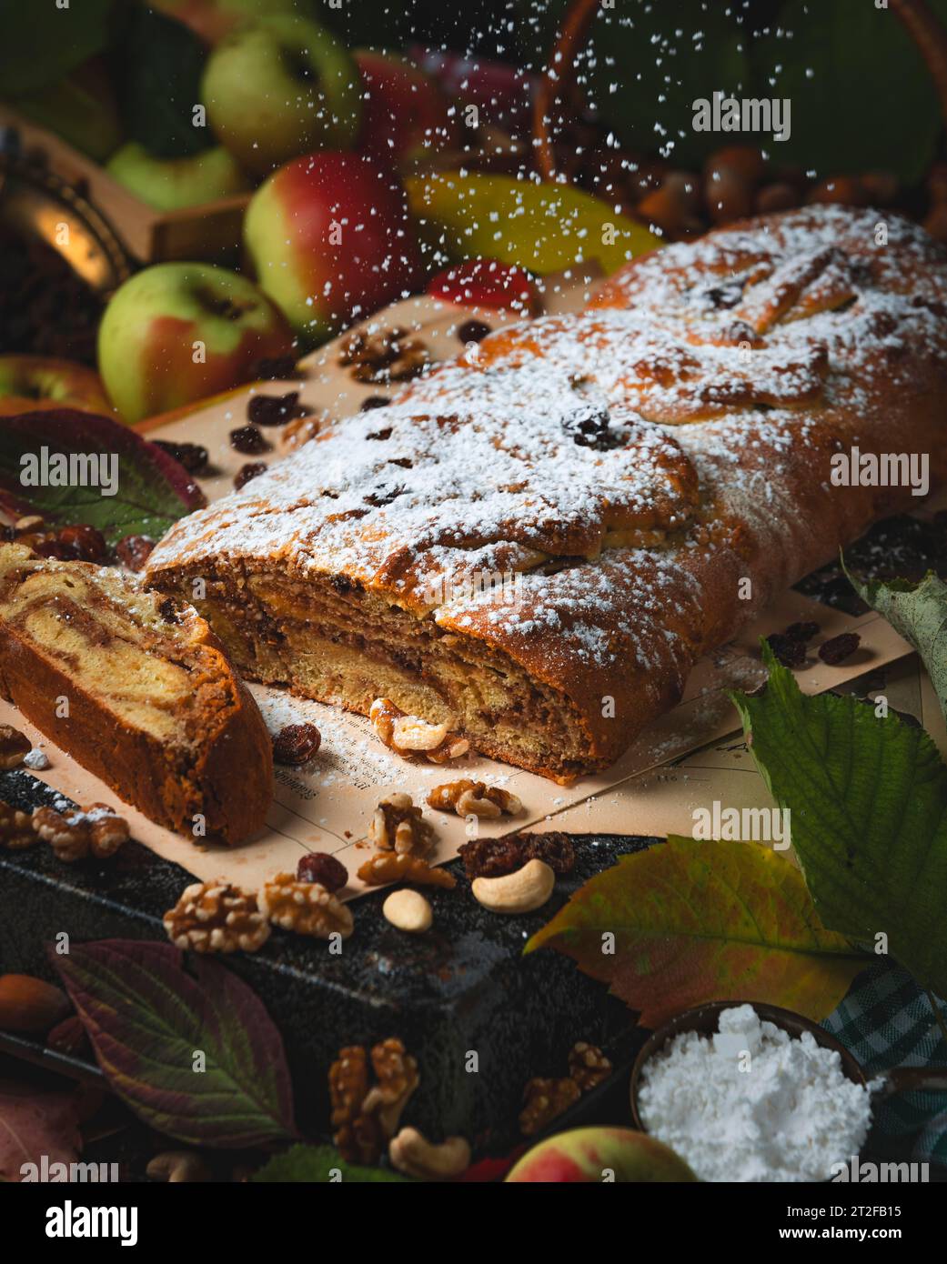 Staubzucker fällt in herbstlicher Atmosphäre auf Nussstrudel, Haselnüsse, Nüsse, Blätter, Äpfel, Lebensmittelfotografie Stockfoto
