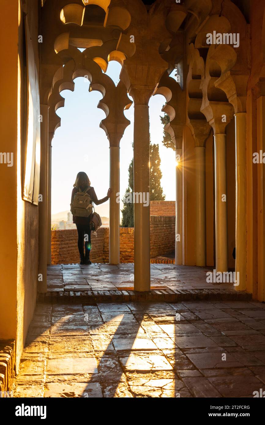 Eine junge Frau bei Sonnenuntergang von den arabischen Türen eines Hofes der Alcazaba in der Stadt Malaga, Andalusien. Spanien. Mittelalterliche Festung auf arabisch Stockfoto