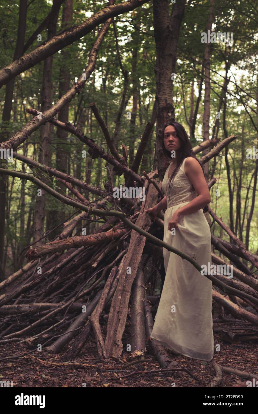 Eine Frau in einem weißen Kleid im tiefen Wald, eine Hexe, eine wilde Frau, die im Wald lebt, ein klassisches weißes Kleid Stockfoto