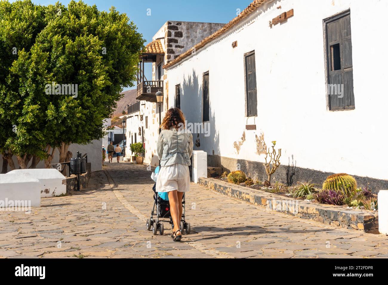Eine junge Mutter, die neben der weißen Kirche von Betancuria, der Westküste der Insel Fuerteventura, den Kanarischen Inseln, spaziert. Spanien Stockfoto