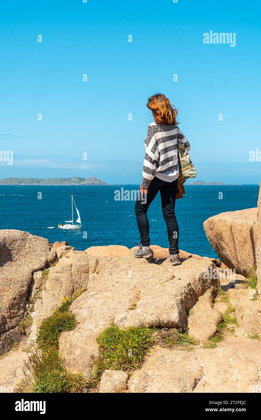 Eine junge Frau am Meer an der Küste neben dem Leuchtturm Mean Ruz, Hafen von Ploumanach, in der Stadt Perros-Guirec, Cotes-d'Armor, auf Französisch Stockfoto